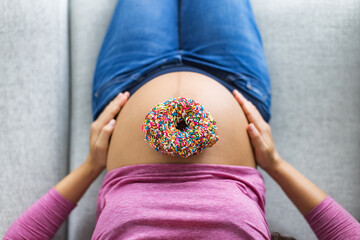 Pregnant woman with donut on belly top view. Cravings of desserts and sweets during pregnancy, Pastry with birthday cake sprinkles on baby bump for gestational diabetes