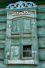 Wall of an old dilapidated log house with a closed window. Carved platbands and dilapidated shutters