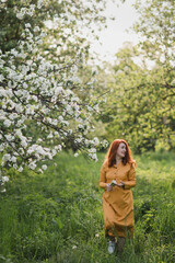 Portrait of gorgeous middle aged woman in casual dress relaxing in a blooming spring garden. Happy senior woman smiling and looking at camera. Red-haired mature lady posing outdoors in a spring day.
