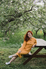 Portrait of gorgeous middle aged woman in casual dress relaxing in a blooming spring garden. Happy senior woman smiling and looking at camera. Red-haired mature lady posing outdoors in a spring day.