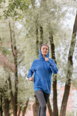 a European woman in a blue hoodie is running and doing sports in the park. selective focus, fitness and yoga outdoor sports, exercise and meditation and fitness for body health. spiritual development