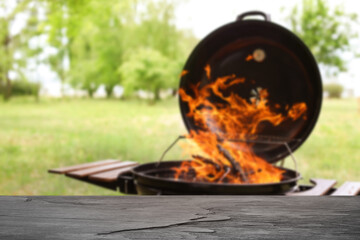 Empty wooden table and blurred view of modern barbecue grill with fire flames outdoors