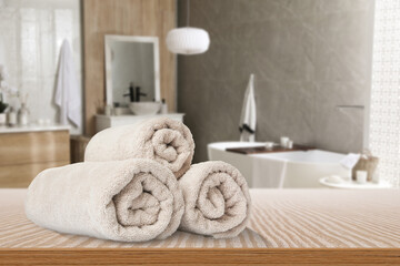 Rolled beige towels on wooden table in bathroom. Space for text