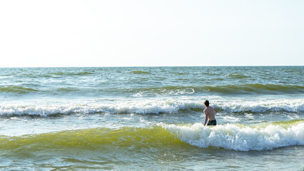 Teenager or a young man enters the waves with white foam on the Baltic Sea, Curonian Spit,...