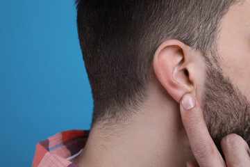 Man pointing at his ear on light blue background, closeup - obrazy, fototapety, plakaty