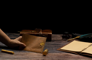 woman's hands, person showing an envelope with a stamp marked in wax holding a leather notebook with a pen and ink bottle.