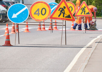 Road signs, and traffic cones with orange and white stripes in background, and standing on road....