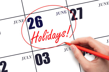 Hand drawing a red circle and writing the text Holidays on the calendar date 26 June. Important date.