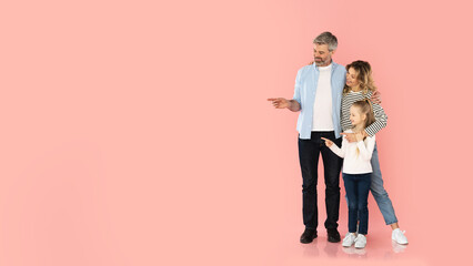 Cheerful Parents And Little Daughter Pointing Fingers Aside, Pink Background