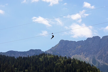 fearless person hanging from the steel cable that connects the opposite slopes of the mountain and the force of gravity that drags down