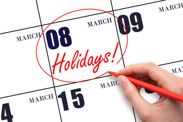 Hand drawing a red circle and writing the text Holidays on the calendar date 8 March. Important date.