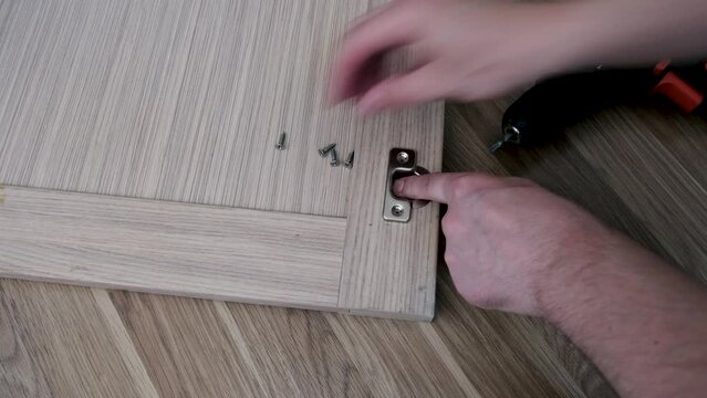 In the kitchen, the carpenter attaches the cabinet door hinges with an electric screwdriver.