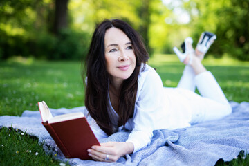 Eine Frau liegt auf einer Decke im Park und liest ein Buch 