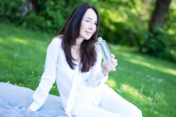 Frau im mittleren Alter in der Natur trinkt Wasser aus einer Wasserflasche 