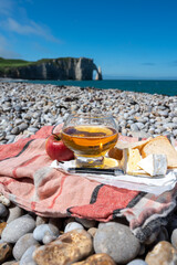 Lunch on pebbles beach of Etretat, french cheese camembert and apple cider drink with chalk cliffs and Atlantic ocean on background, Normandy, France