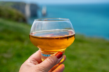 Woman's hand with glass of apple cider drink and view on  on green grass fields on chalk cliffs of...