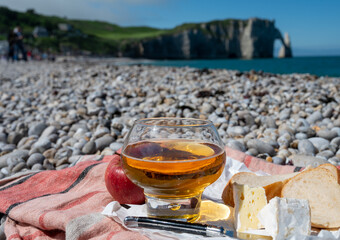 Lunch on pebbles beach of Etretat, french cheese camembert and apple cider drink with chalk cliffs and Atlantic ocean on background, Normandy, France