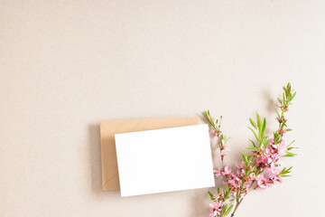 The layout consists of a kraft envelope with blank paper and a delicate branch of pink flowers on a beige background.