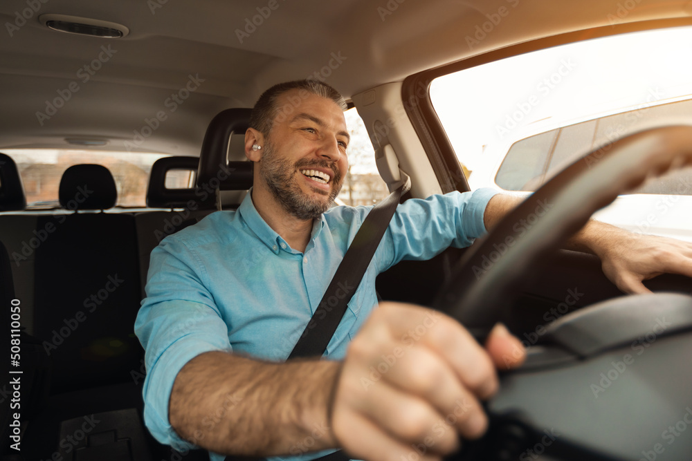 Wall mural Happy man in earphones enjoying music driving luxury car