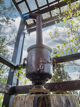 Vintage style russian samovar on the table on the patio of a country house. Water poured into the samovar is heated by the fire burning in the inner pipe. 