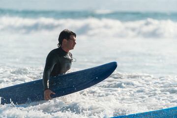 young latin surfer walking in the sea with the surfboard towards the waves