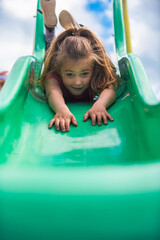 Happy kid girl riding down on a slide at the playground while playing in the summer park.