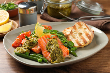 Tasty cooked salmon with pesto sauce served on wooden table, closeup
