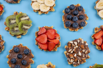 background of appetizing sweet wafers with chocolate spread, nuts and fruits on a blue background. Summer, bright, trendy background, food design