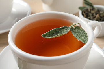 Cup of aromatic sage tea with fresh leaves on table, closeup