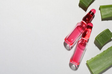 Pharmaceutical ampoules with medication and aloe leaves on light background, flat lay. Space for...