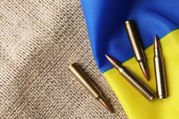 Bullets and national Ukrainian flag on burlap, flat lay. Space for text