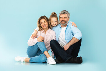 Fototapeta na wymiar Cheerful Family Of Three Embracing Posing Together On Blue Background