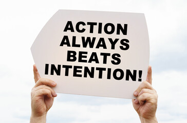 Against the background of the sky in the hands of a man is a sign with the inscription - ACTION ALWAYS BEATS INTENTION