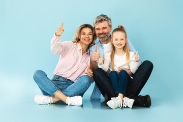 Happy Family Gesturing Thumbs Up Smiling Sitting Over Blue Background