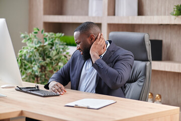 CEO gets neck problems at workplace. African American in a business suit Office worker sour muscles and neck pain. Health problems at workplace.