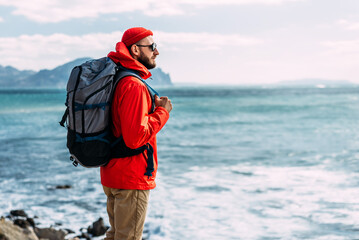 Tourist with a backpack on the background of the sea, rear view. A man in tourist gear on the...