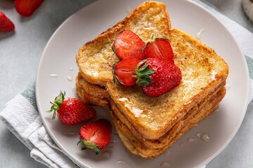 Traditional french toasts with strawberries and honey on grey background. Summer breakfast, brunch or lunch with berries. Selective focus.