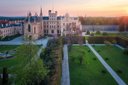 Aerial, over the garden view of Lednice Castle, Moravia, Czechia. Famous tourist spot. Fairytale castle in a baroque garden, lit by the morning sun. UNESCO cultural heritage.