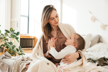 Lovely portrait of mother and daughter. A little girl hugs her mother in a bright bedroom. An adult woman enjoys love from her daughter. Mothers Day