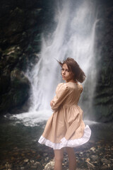 Young beautiful girl in a dress on the background of a waterfall.