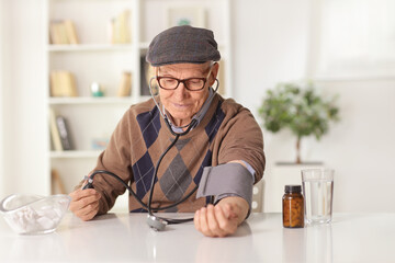 Elderly man checking blood pressure at home with pills in a bottle