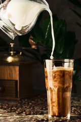 Milk is poured into coffee, making coffee latte or iced coffee in a glass. Vertical shot, selective focus