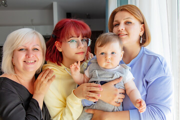 Four ukraininan women, senior, teen and adult with infant child stand near window at home