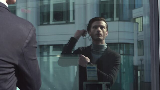 The businessman is adjusting suit and hairstyle, an outside mirrored window