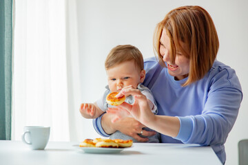 Ukrainian migrant mother with infant daughter sit at table with cheesecake on breakfast