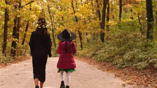 Back view video of two girls walking in the forest among the trees wearing costumes ready for the Halloween party.