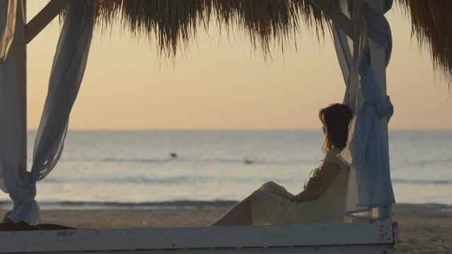 Single woman sit in canopy and admire sea and sunset sky, quiet, calm, summer peace