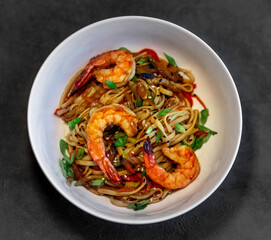Asian udon noodles with shrimp, vegetables and teriyaki sauce on a black concrete background. Chinese and Japanese cuisine.