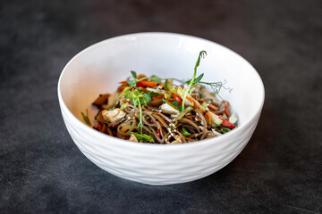 Asian udon noodles with chicken vegetables and teriyaki sauce on a black concrete background.