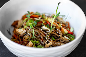 Asian udon noodles with chicken vegetables and teriyaki sauce on a black concrete background.